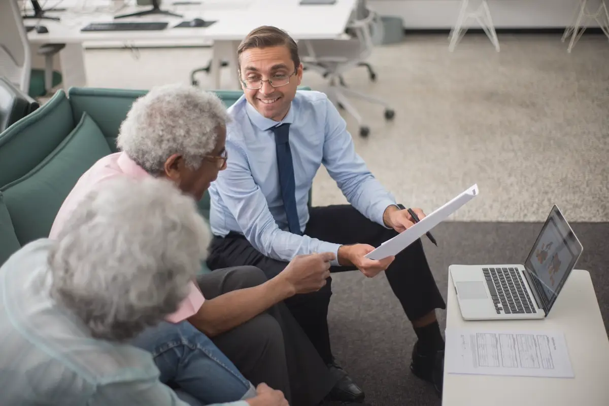 Consultor conversando com um casal de idosos e mostrando um documento sobre as finanças deles