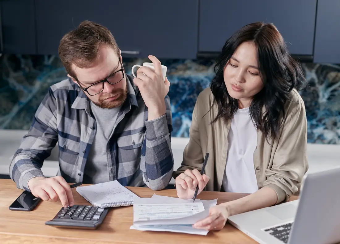 Casal revisando contas e boletos com uma calculadora na mesa da cozinha